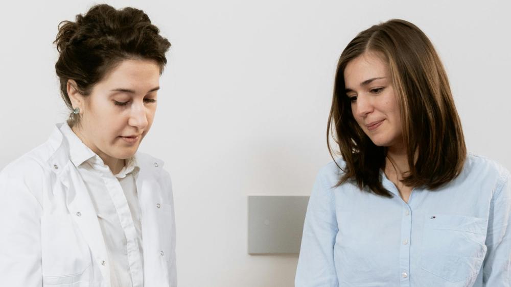 A clinical healthcare professional sits with a patient.