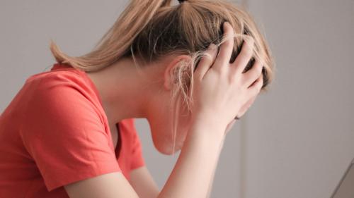 A person has their head in their hands whilst looking at a laptop. 