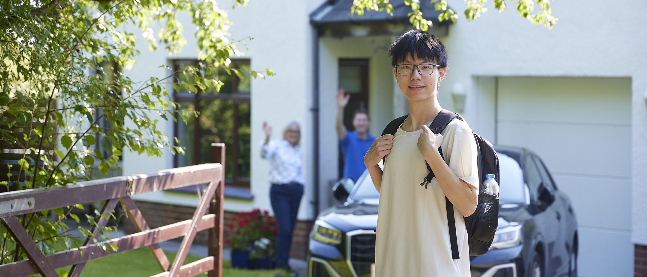 International student outside a home with hosts waving from the door